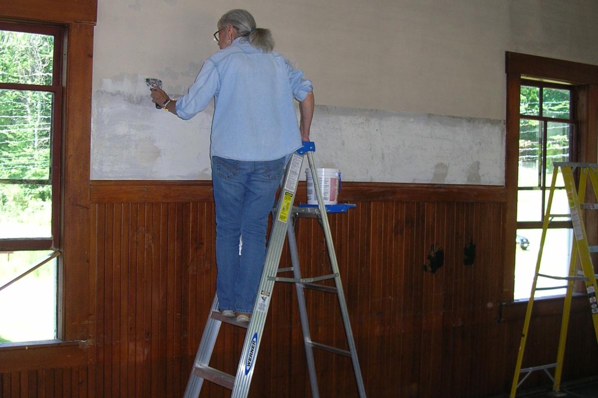 Volunteer Ann Xavier, who serves on the Heritage Commission, applies some spackle.  Notice the 2 black area of old blackboard cement on the wainscott.  Now you see them...