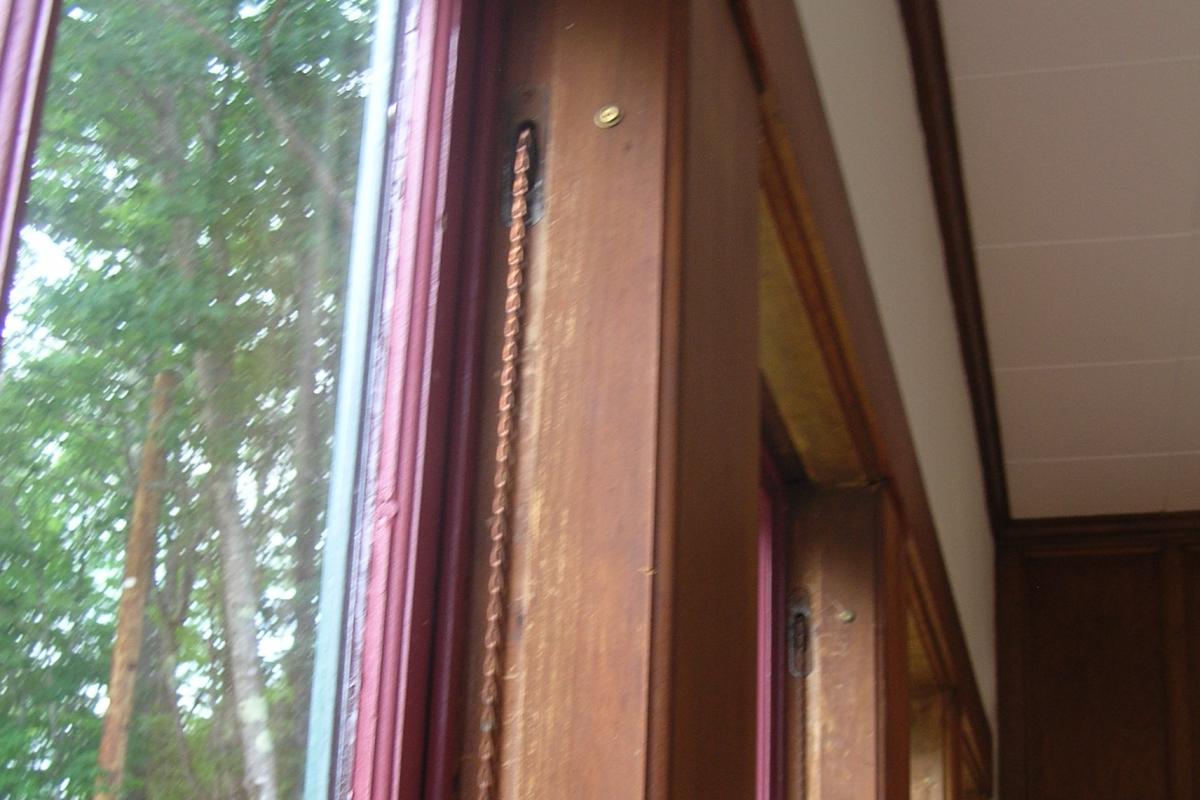 Close-up photo of a new window chain, which is threaded over the top of an original window pulley wheel.