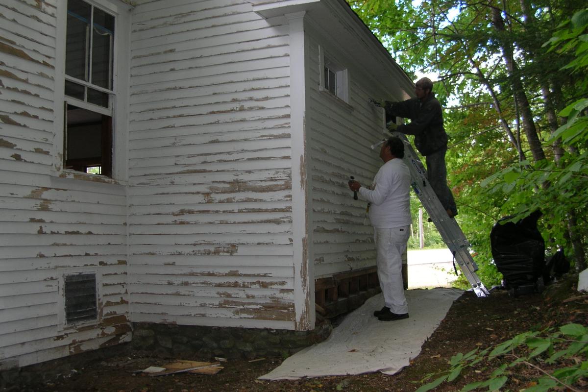 Painting begins with gentle hand-scrapping to prepare the surface without damaging the old clapboard.
