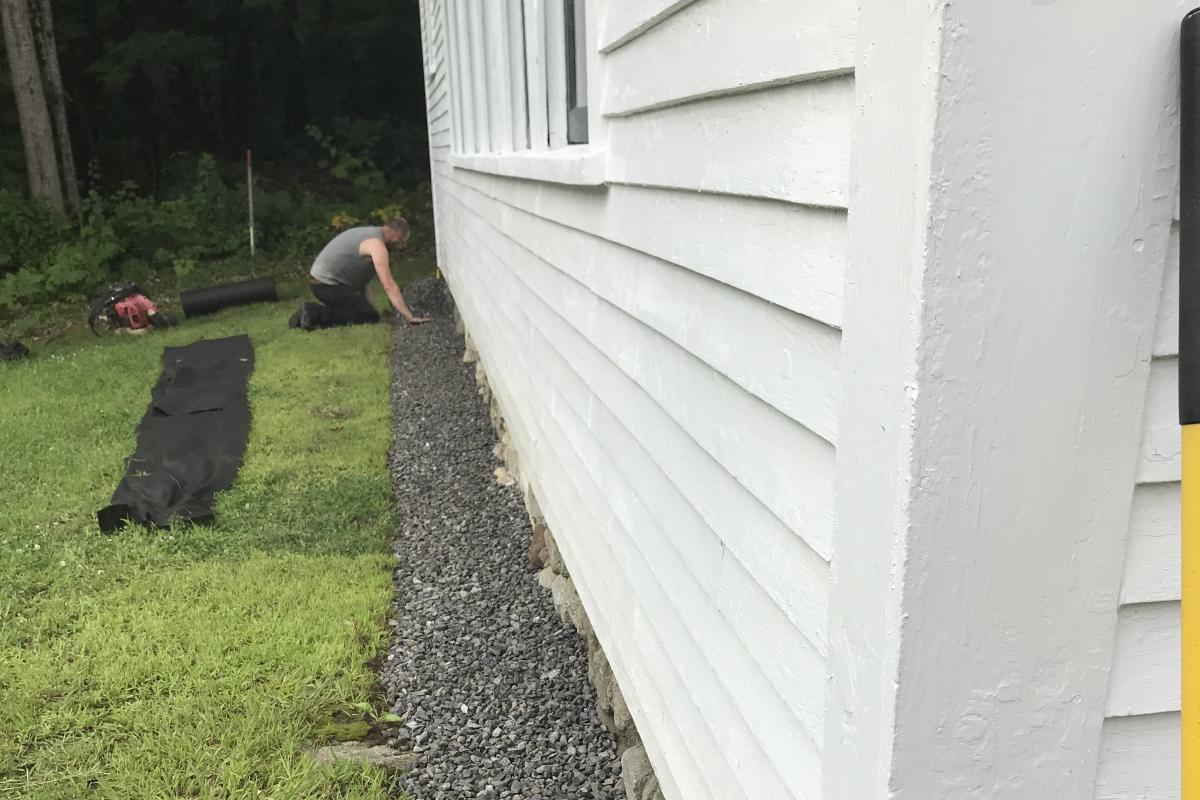 August 22, 2019 - To protect the clapboard, fractured stone is being laid over a fabric barrier aroumd the Town House.